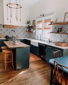 a kitchen with wooden floors and black cabinets, an island in the middle is surrounded by chairs