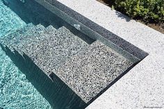 an aerial view of a swimming pool with blue water and rocks on the ground, surrounded by greenery