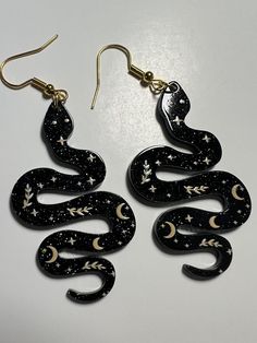 Magic Snake Earrings    Gorgeous glittery black acrylic snake earrings with moon, stars and plant design in a gold colour. They shine beautifully.  5cm tall, 2.8cm wide and 2mm thick charms on gold metal dangling earring hooks.  Brand new items in their original packaging.  Check out the photos for a great view of the item.  Age 6+. Mystical Black Jewelry For Party, Handmade Black Magical Jewelry, Handmade Magical Black Jewelry, Black Celestial Earrings For Gift, Black Celestial Dangle Earrings, Black Resin Dangle Jewelry, Black Resin Party Jewelry, Magic Snake, Spiritual Nature