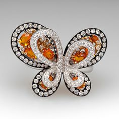 This exquisite butterfly ring is accented with seven (7), prong set, oval mixed cut natural spessartine garnet, two (2), prong set, round mixed cut natural spessartine garnet and one hundred forty-seven (147), bead/prong set, round brilliant cut diamonds. The ring measures 21.7mm at the top, rises 10.2mm above the finger, tapering to 3.5mm wide and 1.1mm thick at the base of the shank. This ring is currently a size 8.25. Luxury Butterfly Ring For Formal Occasions, Luxury Butterfly Ring For Wedding, Diamond Butterfly Ring With Gemstone For Formal Occasions, Formal Diamond Butterfly Ring With Gemstone, Luxury White Gold Butterfly Ring, Luxury Butterfly-shaped Ring For Gift, Luxury Butterfly Ring For Gift, Luxury Butterfly Rings For Gifts, Luxury Butterfly Rings For Gift