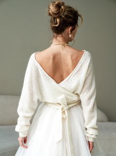 the back of a woman's white dress with a long sleeved sweater on