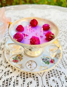 a bowl filled with flowers on top of a white doily covered table next to a pink candle