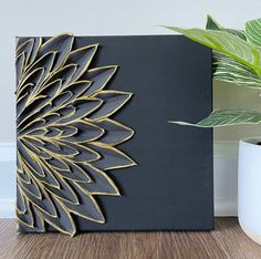 a black and gold canvas with a plant in the corner next to it on a wooden floor