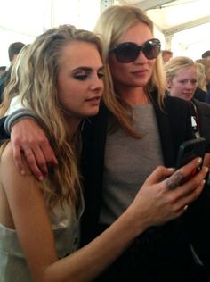 two beautiful women standing next to each other while looking at a cell phone in front of them