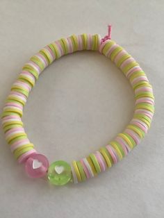 a pink, yellow and green beaded bracelet on a white surface with a heart charm