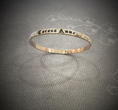 MAKE SURE OF THE SIZE BEFORE ORDERING. 5mm gold filled Hawaiian bangle, 1.70mm thickness. Personalize it with a name or a message engraved and enameled in black. The pattern of plumerias and Victorian scrolls are rolled on a 5mm barrel gold filled wire. All the characters are engraved , not stamped, resulting in straight and aligned name. A black enamel is used to fill in the characters engraved. The maximum number of letters is 15. How Gold filled is made. Gold filled or gold overlay is made by Adjustable Gold Bangle With Engraving Option, Engraved Name Bangle Bracelet For Anniversary, Engraved Name Bangle For Anniversary, Gold Bangle With Engraved Text, Personalized Name Gold Bangle, Personalized Gold Stamped Name Bracelet, Personalized Stamped Gold Name Bracelet, Gold Name Bangle For Anniversary, Customizable Gold Bangle For Anniversary