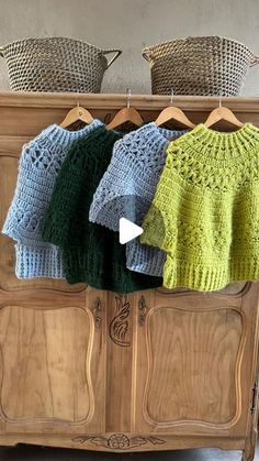 three knitted sweaters are hanging on a clothes rack in front of a dresser