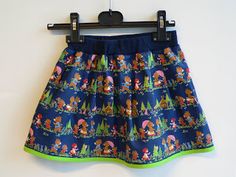 a skirt hanging up on a wall with cartoon characters all over it and trees in the background