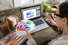 a woman sitting at a table with a laptop and color swatches in front of her