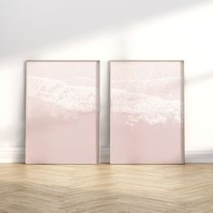 two pink framed pictures sitting on top of a wooden floor next to a white wall