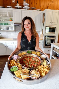 a woman holding a platter full of food with the words epic chili dinner board