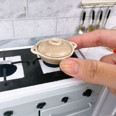 a hand is holding a small bowl on top of a stove