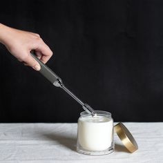 a person using a knife to cut into a glass jar filled with white liquid on a table