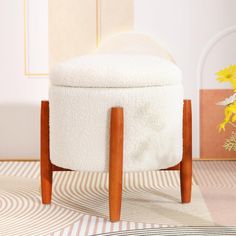 a white ottoman sitting on top of a rug next to a vase with yellow flowers