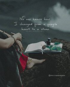 a person sitting on top of a rock with a book and pen in their lap