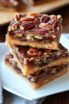 three pieces of pecan bar stacked on top of each other with chocolate and pecans