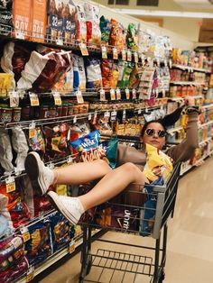 a woman sitting in a shopping cart at a grocery store with her feet on the ground