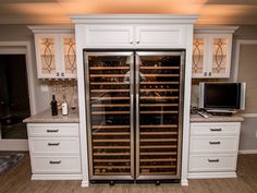 a wine cellar in the middle of a kitchen with white cabinets and marble counter tops