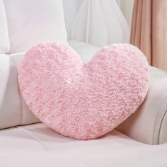 a pink heart shaped pillow sitting on top of a white couch