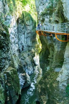 a man standing on a bridge over a river next to a cliff with a canyon below