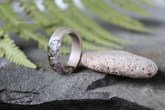 two wedding rings sitting on top of a rock next to a fern leaf and stone