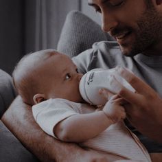 a man holding a baby in his arms and looking at the bottle he is holding