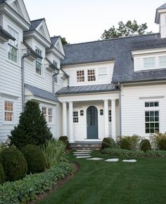 a white house with green grass and bushes in front of the door is surrounded by trees and shrubbery