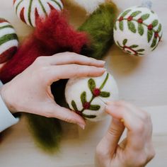 two hands are decorating christmas balls on a table