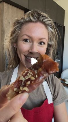 a woman in an apron holding up a piece of food to the camera and smiling