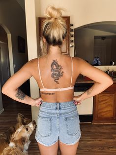 a woman with a dragon tattoo on her back standing next to a dog and looking at the camera