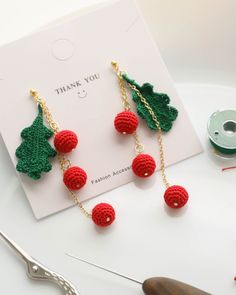 red and green crocheted christmas tree earrings with gold chains on white table next to sewing thread