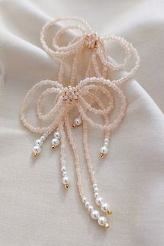 a white fabric with pearls and gold beads on the side, as well as a bow brooch