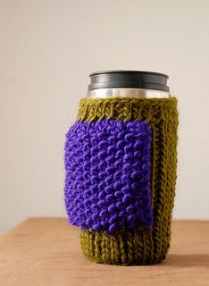 a knitted coffee cup cozying in purple and green with a black lid on a wooden table