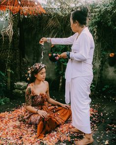 two women sitting on the ground with leaves all over them and one woman pouring water into her face