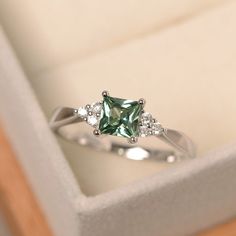 an engagement ring with green and white stones in a box on top of a wooden table