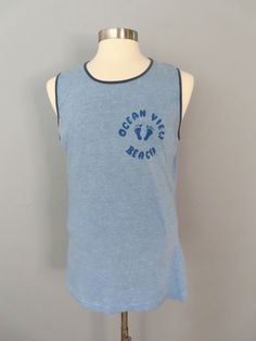 Vintage sleeveless t-shirt. Blue heather with dark blue trim around the neck and sleeves. Graphic on right breast Ocean View Beach with foot prints.  MEASUREMENTS--Taken with garment laying flat, in inches, doubled: Shoulder: 15.5" Chest: 44" Waist: 38" Overall length from shoulder to hem: 29.5" Label/ Era: Hanes | 1980 Fabric: Cotton, polyester Condition: Great condition. Cleaned and ready to wear.  ★ Shop entire shop here: https://www.etsy.com/shop/retrosuzysvintage Instagram | retrosuzysvintage Facebook | retrosuzysvintage Vintage Beach Shirt With Vintage Print, Vintage Summer Beach T-shirt, Blue Vintage Beach Shirt, Vintage Graphic Print Beach T-shirt, 90s Cotton T-shirt For Beach, Ocean Views Beach, Sleeveless Tshirt, Ocean View, Overalls