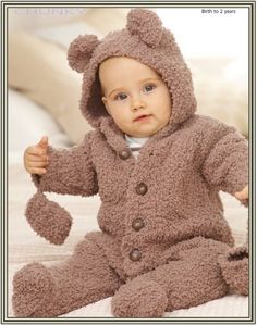 a baby in a bear suit sitting on a bed