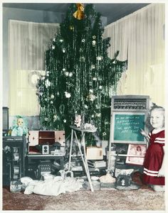 an old photo of a child standing in front of a christmas tree