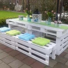 an outdoor table made out of pallets with green and blue towels on it, in the middle of a garden