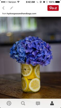 a glass vase filled with lemon slices and blue hydrangeas on top of a wooden table