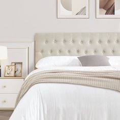 a bed with white linens and two pictures on the wall above it in a bedroom