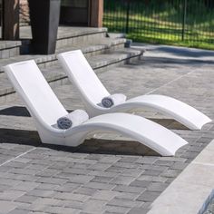 two white lounge chairs sitting next to each other on a brick walkway in front of a building