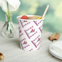 a paper cup with strawberries in it sitting on a table next to plates and flowers