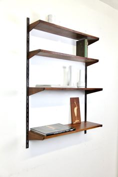 two wooden shelves with books and vases on them against a white wall in a room