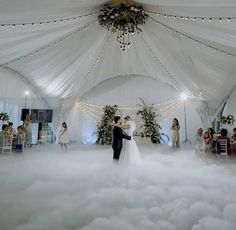 a bride and groom are dancing in the middle of a cloud filled room with chandeliers