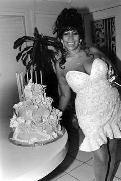 a woman standing next to a cake on top of a kitchen floor covered in white frosting