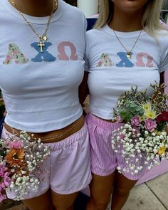 two women wearing matching shirts and shorts with flowers in their lapel holes, both holding bouquets