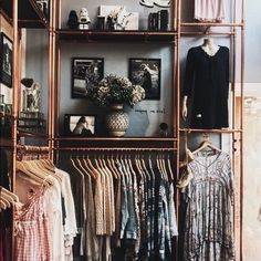 an open closet with clothes on shelves and pictures hanging from the wall behind it,