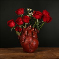 a heart shaped vase filled with red roses on top of a wooden table in front of a black background