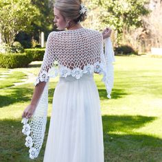 a woman wearing a white crochet wedding dress and shawl in the grass